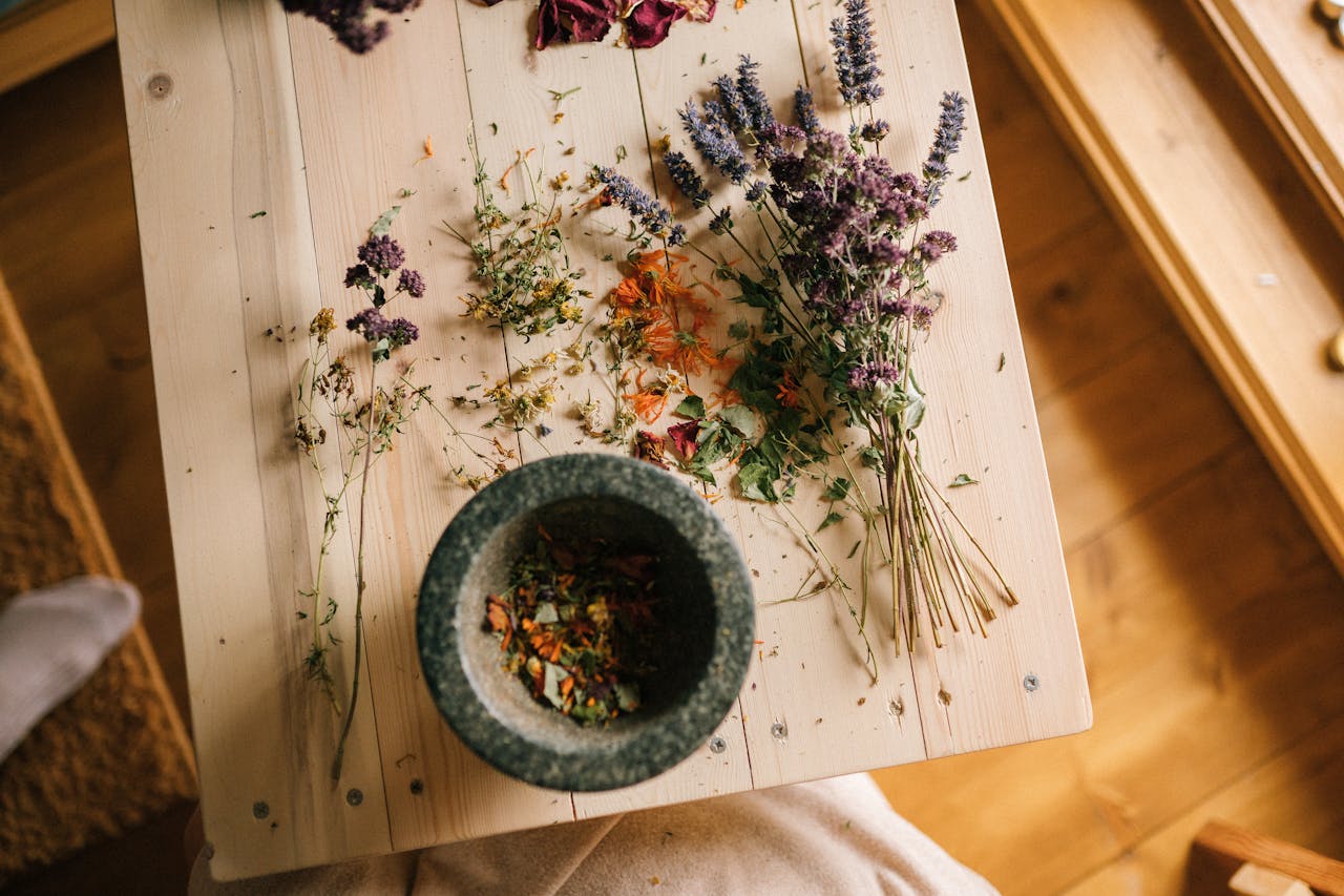 Dried herbs and flowers arranged on a wooden table with a stone mortar for home remedies.